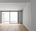 Large open space with white walls, wooden floor, and sliding glass doors leading to a balcony or terrace