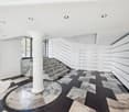 modern interior, white walls, black and white checkered floor, central column, staircase, white ceiling with recessed lighting