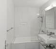 modern bathroom with white tiles, bathtub, shower, sink, mirror, and a glass door