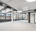 An empty office with white ceiling, large windows with city view, glass wall, carpeted floor, pillar in the middle