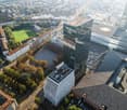 Aerial view of buildings with large windows, multiple buildings with green roofs, surrounded by trees, and a wide avenue