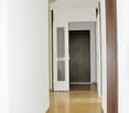 Empty hallway with white walls, wooden floor, two doors, one with glass panel