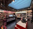 Cosmetics store with various brands displayed on shelves, a central counter with a computer, and a signboard with the text 'MAKE-UP'.