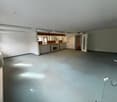 Large open-plan room with white walls, concrete flooring, and built-in kitchen cabinets and appliances. The room appears to be a combination of a living area and a kitchen space.