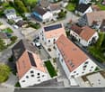 Aerial view of a residential area with multiple houses, some with solar panels on the roofs, brown roofs, and a mix of architectural styles.