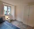 bedroom with bed, nightstand with lamp, wardrobe, window with outdoor view, beige walls, tiled floor