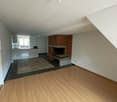 Open-concept living room with hardwood flooring, a brick fireplace, and a kitchen area with tile flooring