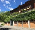 a wooden building with multiple garage doors and a balcony on top, surrounded by greenery