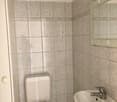 A small bathroom with tile walls, white sink, toilet, mirror, and a faucet
