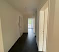 Empty hallway with black tiles, white walls, doors, and a balcony