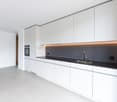 modern kitchen with white cabinets, black countertops, stainless steel sink, built-in oven, under-cabinet lighting