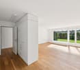 empty room, wooden floor, white walls, large windows, kitchen area with sink and stove
