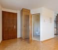 Empty room with wooden door, wooden cabinet, open door to bathroom, wooden floor, white walls