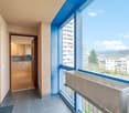Balcony with blue railings, wooden floor, kitchen with cabinets and microwave, view of the city