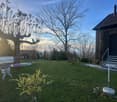 Well-maintained garden with a variety of plants, neatly trimmed grass, trees, a swing set, and a building with a shingled roof.