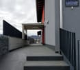 Exterior of a building with a raised ground floor, concrete steps, metal railings, and a sign reading 'LACHAT construction Sàrl'.