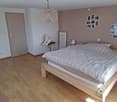 Bedroom with wooden floor, bed, lamp, stuffed toy, radiator, door, mirror, photo frames on the wall