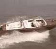 A vintage-style wooden speedboat speeding across the water, with people seated inside the boat.