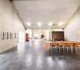Large open space with concrete walls and ceiling, wooden dining table with chairs, fireplace, and various decorative elements throughout the room