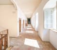 long corridor, white walls, brick floor, arched ceiling, doors, windows, wooden railing