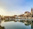 Picturesque town with historic buildings, a river, and a covered bridge. The town has a medieval or old-world charm with its architecture and scenic setting.