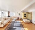 Living room with white walls, wooden floor, large windows, two sofas, coffee table, fireplace, rug, decorative items