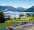 Outdoor scene with a house, lake, mountains, trees, grass, and machinery vehicles