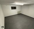 Empty room with white walls, gray tiled floor, small window, and a radiator
