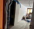 Concrete walls, grey tiled floor, exposed pipes and cables, storage boxes and tools scattered around.