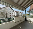Balcony with green railings, tiled floor, white walls, awning, planter box, view of surrounding buildings