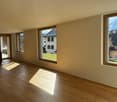 Spacious empty room with large windows, wooden floors, kitchen, mountain view