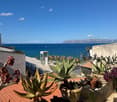 Red roof, multiple potted plants, sea view, buildings and mountains in the distance