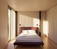 A bedroom with a large bed, white walls, wooden floor, large windows, and a view of the outside.