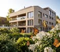 Modern apartment building, multiple floors, large windows, balconies, surrounded by greenery