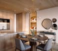 Dining area with a round wooden table, 4 chairs, a chandelier, a kitchen with a sink, a counter, and a wooden cabinet, a mirror, and a small bedroom