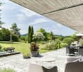 Stone patio, outdoor furniture, potted plants, garden view, grassy lawn, trees, seating area