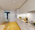 modern kitchen with white cabinets, wooden floor, induction stove, sink, dishwasher, washing machine, countertop, kitchen utensils, vegetables