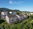 Multiple story building, with balconies, located in a hilly area with mountains in the background