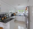 modern kitchen with white cabinets, black granite countertop, stainless steel appliances, wooden stool, open door to the garden