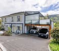 2 story house, white exterior, glass garage, 2 cars parked, bicycles, paved driveway