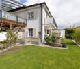 2 story house, white exterior, glass windows, balcony, garden with grass and plants