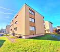 Multi-story apartment building, brick, windows, paved path, green lawn, parked car