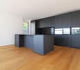 modern kitchen with island, black cabinets, wooden floor, white walls, glass door, stainless steel appliances