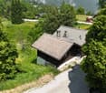 A traditional alpine-style wooden house surrounded by lush green trees and vegetation, situated in a picturesque mountain landscape.