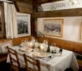 Rustic wooden interior with a dining table set for a meal, framed mountain landscape artwork on the wall, and a sign that says 'Cusching'