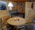 Rustic wooden dining table and chairs, stone fireplace, hanging light fixture, decorative fruit and floral arrangements, wooden walls and ceiling