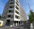 Multi-story apartment building with balconies, concrete and glass construction, parking area in front