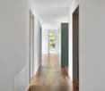 White walls, wooden floor, bright view from the end of the hallway.