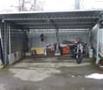 Sheltered carpark with two stone lion statues on both sides, motorcycle, barrels, trolley and buckets.