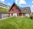2 story house, red panels, red roof, beige basement, grassy lawn, outdoor chairs, modern design